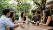 © Pimnon - Five friends enjoy drinks and conversation at a rustic outdoor cafe surrounded by greenery on a sunny day.