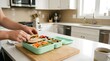© Olinka N - A person prepares a lunch box with sandwich, fruits, and vegetables in a bright kitchen. The setting shows a clean countertop and sunlight coming through the window