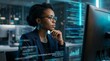 © Gophotograph - Focused black woman wearing glasses concentrating on complex data and code on a computer screen.