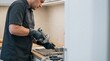 © Rustic Touch - Professional plumber using a drain snake tool to clear a kitchen sink clog at home.