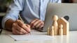 © Soyaeb - Man signing home insurance or mortgage contract with wooden family figures