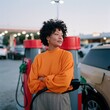 © Andrii Zastrozhnov - Woman in orange sweater at gas station fueling car at dusk for background and lifestyle use