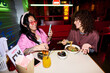 © Mediaphotos - Diverse young adult women eating Asian food in cafe while using smartphone, representing friendship and urban lifestyle, suitable for food delivery and social media marketing campaigns