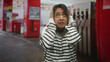 © Krakenimages.com - Hispanic woman covering ears with hands at a gas station near fuel pumps, striped sweater, worried grimace in a roadside forecourt; anxiety unease alarm.