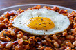 © OlegD - Fried egg on top of savory stewed white beans with tomato sauce and herbs, close up. Delicious breakfast of sunny side up egg served over warm seasoned white bean skillet with vegetables and spices