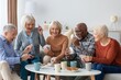 © Prostock-studio - Smiling Diverse Group Of Seniors, Including Men And Women, Engaging In Card Game Together At Home, Sitting In Living Room, Creating Joyful Atmosphere, Celebrating Friendship And Fun.