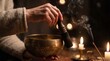 © Darakorn - Close up of hands playing a Tibetan singing bowl with a wooden mallet, surrounded by warm candle light and burning incense smoke during a sound therapy and meditation session.