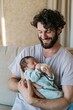 © Andrii Zastrozhnov - Young father feeding newborn with a bottle on a sofa for parenting banner and family lifestyle background