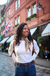 © CarlosBarquero - Vertical. Smiling Black Latina tourist exploring a cobblestone street in London with a British flag behind. Vertical travel portrait conveying confidence, curiosity and enjoyment during a city break.