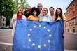 © CarlosBarquero - Multiracial group of friends holding the European Union flag with pride, symbolizing unity and diversity. Joyful atmosphere outdoors, promoting togetherness and cultural harmony in a vibrant setting