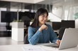 © fizkes - Smiling young Chinese professional woman, office employee using laptop sit at desk at contemporary workplace, reading received business proposal, lead correspondence to client, engages in online tasks