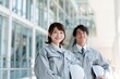 © Arch & Human Studio - 作業服姿の男女エンジニアがヘルメットを抱え笑顔で未来を見据える