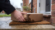 © Art_spiral - Hand picking up wet water damaged cardboard delivery box from outside doorstep doormat in front of house after rain shipping package problem