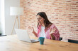 © Daniel - Young woman looking at her laptop screen with an excited expression and open hands, having a remote meeting or receiving good news while working from home