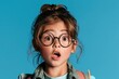 © Olena - Cheerful Child with Glasses in a Blue Studio Backdrop Expressing Surprise and Curiosity About Learning