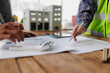 © groviapoto - Architects and engineers collaborating on a building project, reviewing blueprints, making calculations, and discussing design plans for a new development with a building model