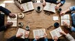 © Zakir - Diverse adults gathering around a wooden table, reading books and enjoying coffee from an overhead view.