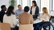 © YuTaus - Group of diverse professionals engaged in discussion around a round table in a modern office setting with large windows and greenery in the background