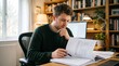 © JorgeEmanuel - Young man focused on reading documents at his desk in a home office with bookshelves