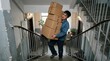 © leonardo - Man carrying heavy stack of cardboard boxes up apartment building stairs