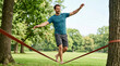 © OlgaNeuroArt - Man balancing on a slackline in a park. Athletic male walking barefoot on a tightrope between trees. Outdoor recreation and balance concept
