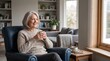 © PSCREATIVE - Smiling senior woman with gray hair holding a mug of coffee while relaxing in a comfortable armchair by the window
