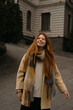 © Aleksandra Gritsenko - Smiling red-haired girl walks down a street in a city during daylight wearing a coat and scarf