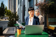 © Davor - Businesswoman reviewing documents on laptop at outdoor cafe
