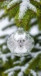 © chaiwat - Elegante pallina di Natale in argento lucido con dettagliate decorazioni a rilievo, sospesa su un ramo di pino verde innevato e sfocato, branch, detail, seasonal