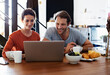 © peopleimages.com - Morning, laptop and couple with breakfast in home for online shopping, website store and internet. Happy, marriage and man with woman with coffee, talking and decision for digital purchase in kitchen