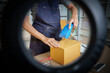 © Natee Meepian - Person Sealing Shipping Box with Tape Seen Through Ring Light Frame