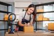 © Natee Meepian - Asian businesswoman writing address on cardboard box for e-commerce order fulfillment