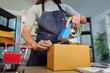 © Natee Meepian - Worker Sealing Cardboard Shipping Box with Tape Dispenser for Online Store
