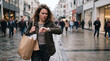© Thumbs - Woman checking watch with shopping bags on busy city street