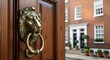 © Faiz Novareza - A traditional brass lion head door knocker attached to a polished wooden entrance showcasing classic architecture and historic charm with a view of residential townhouses on a quiet city street
