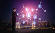 © InfiniteFlow - A professional businessman stands thoughtfully analyzing digital network connections illustrated by icons against a vibrant city skyline during night time. Tessel