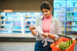 © Serhii - Indian woman checking grocery shopping list in supermarket