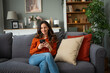 © Jelena - Woman relaxing on sofa using smartphone in living room