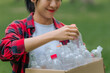© sumitra - Smiling girl in a red plaid shirt holding recyclable pet bottles against a blurry natural bokeh background, ideal for Earth Day and CSR campaigns.
