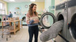 © Thumbs - Woman laughing while loading laundry into a washing machine