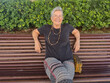 © luciano - Mature adult woman with short gray hair and glasses sitting on a park bench, smiling, enjoying leisure time outdoors and feeling happy in retirement