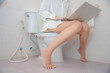 © Thitiporn - Overwork concept showing a busy woman using a laptop while sitting on a toilet in a bathroom, illustrating nonstop work and poor work life balance. overwork, laptop, busy, toilet, multitasking