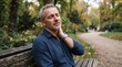 © ardiright - Mature man suffering from neck pain while sitting on a wooden park bench during a relaxing autumn afternoon outdoor stroll