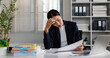 © David - Stressed young asian businesswoman suffering from severe headache and burnout. Feeling overwhelmed by pressure and workload while working in a modern office
