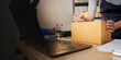 © Natee Meepian - Laptop on desk with cropped worker writing on cardboard package for e-commerce sales