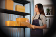 © Natee Meepian - Asian female small business owner holding clipboard to inspect stock on warehouse shelf