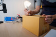 © Natee Meepian - Cropped hands writing address on cardboard box for e-commerce package shipping