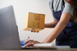 © Natee Meepian - Cropped view of entrepreneur typing on laptop while holding cardboard parcel for e-commerce