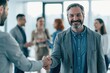 © Khawla - Confident Mature Businessman Smiling and Shaking Hands During Successful Corporate Meeting in Modern Office