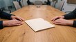 © Biggy - Business Meeting with Two Hands Reaching for a Folder on a Wooden Table in a Conference Room